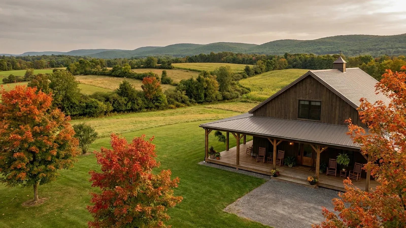 A barndominium exterior showing a deep wrap-around covered porch with posts and railing along two sides of the building.